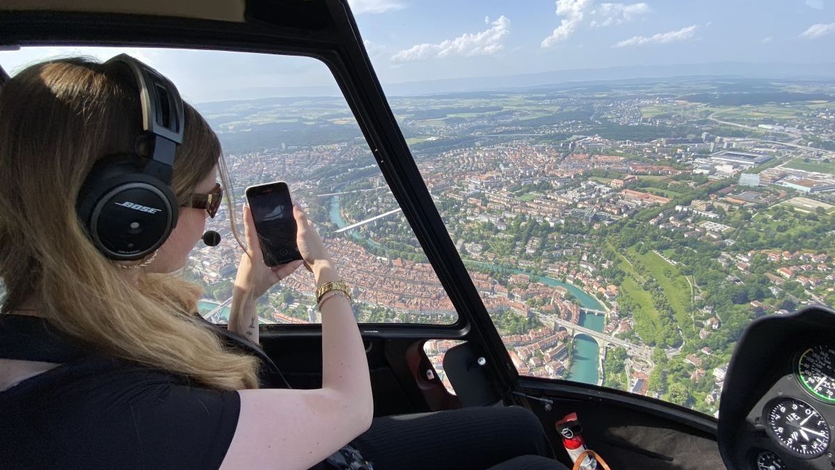 Junge Dame welche aus dem Helikopter-Cockpit die Schweizer Hauptstadt fotografiert.